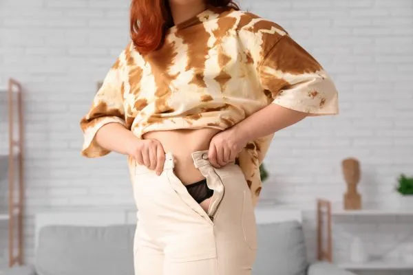 Image of woman trying to do her trousers up after pregnancy weight gain Theale