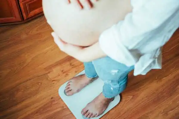 Image of woman weighing herself and experiencing weight gain through pregnancy Theale